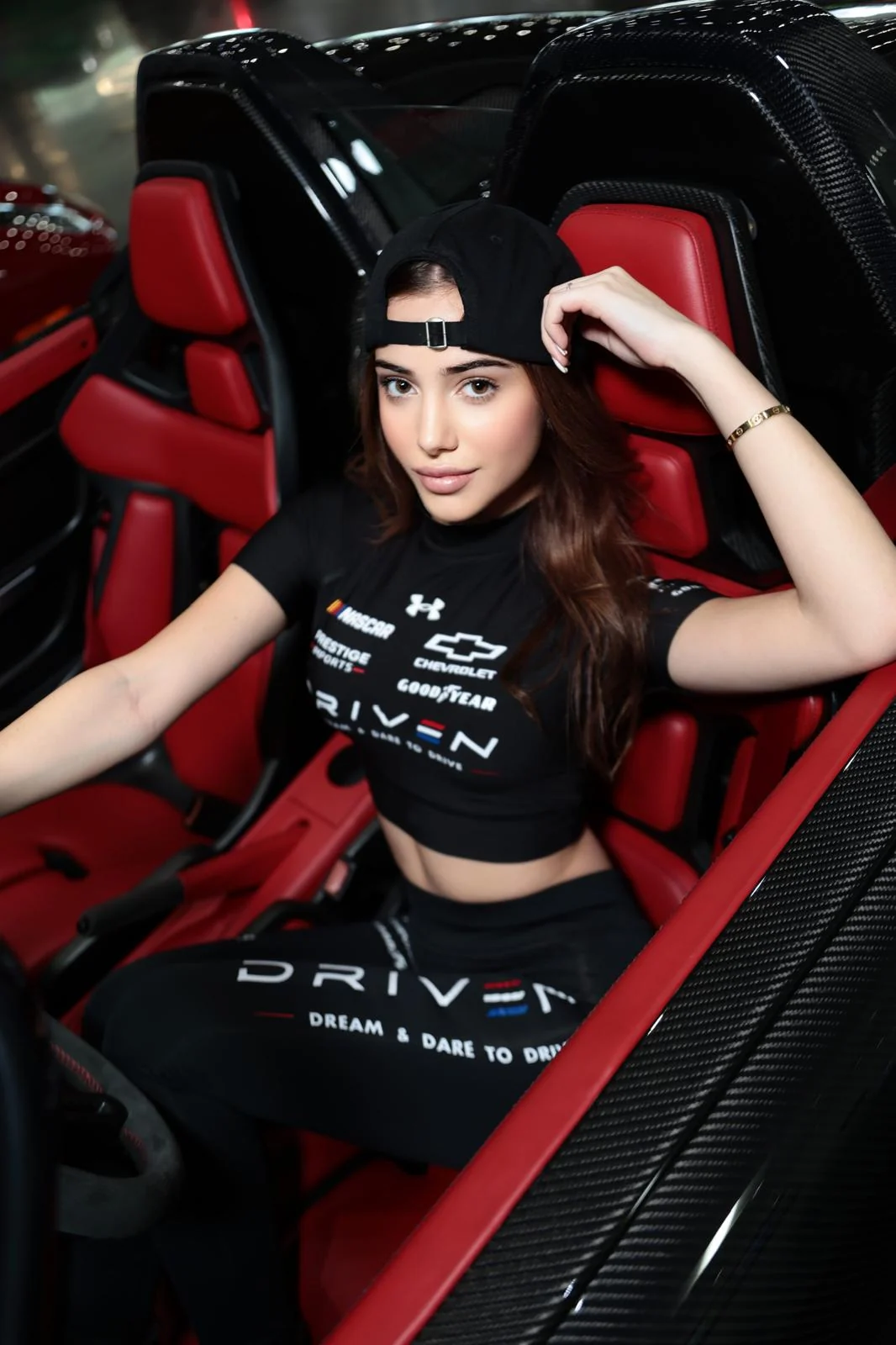 Mila in her black DRIVEN uniform seated in a sports car with red leather seats